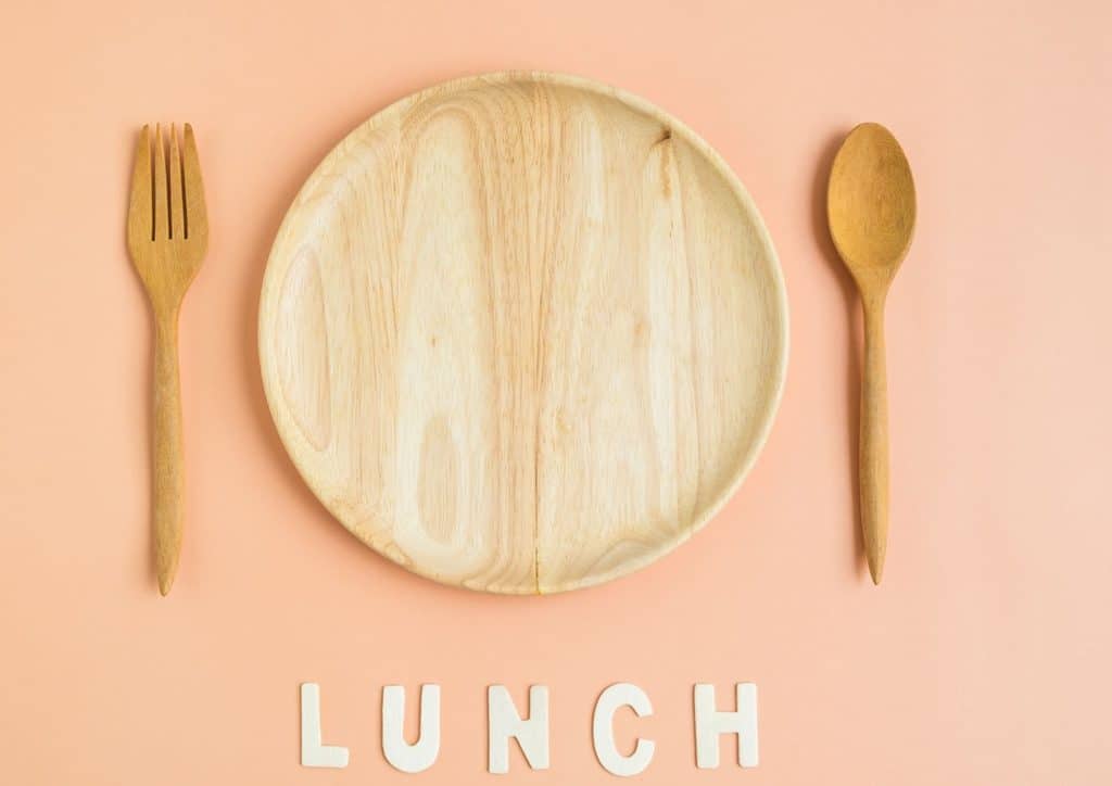 Healthy Lunches for Weight Loss: Work and Home Ideas 1 Wooden plate with fork and spoon arranged on a pink background, representing a lunch concept.