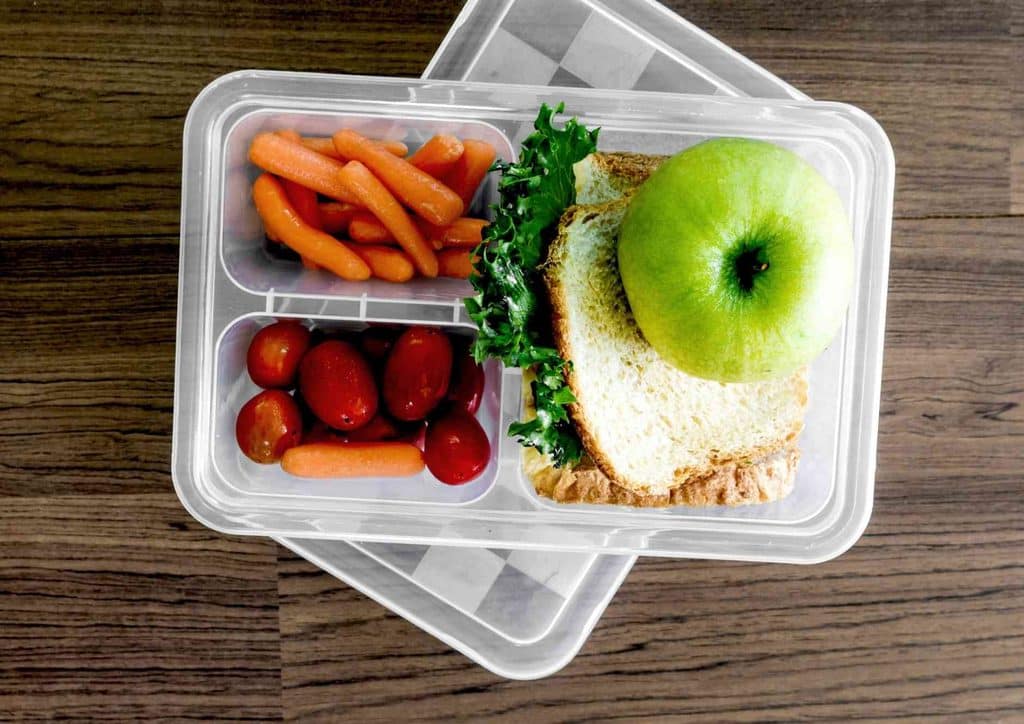 Healthy Lunches for Weight Loss: Work and Home Ideas 5 A lunch box containing a sandwich, baby carrots, and sliced apples arranged neatly inside.