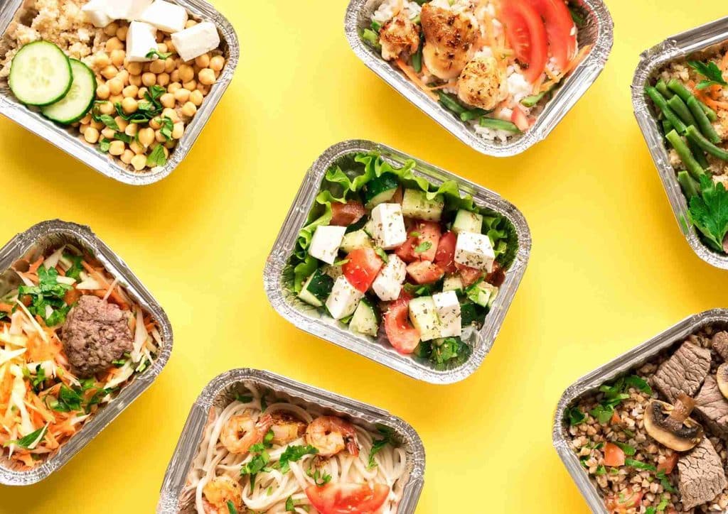 Easy Meals for Weight Loss When You're Short on Time 8 Various food dishes in clear plastic containers displayed against a vibrant yellow backdrop.