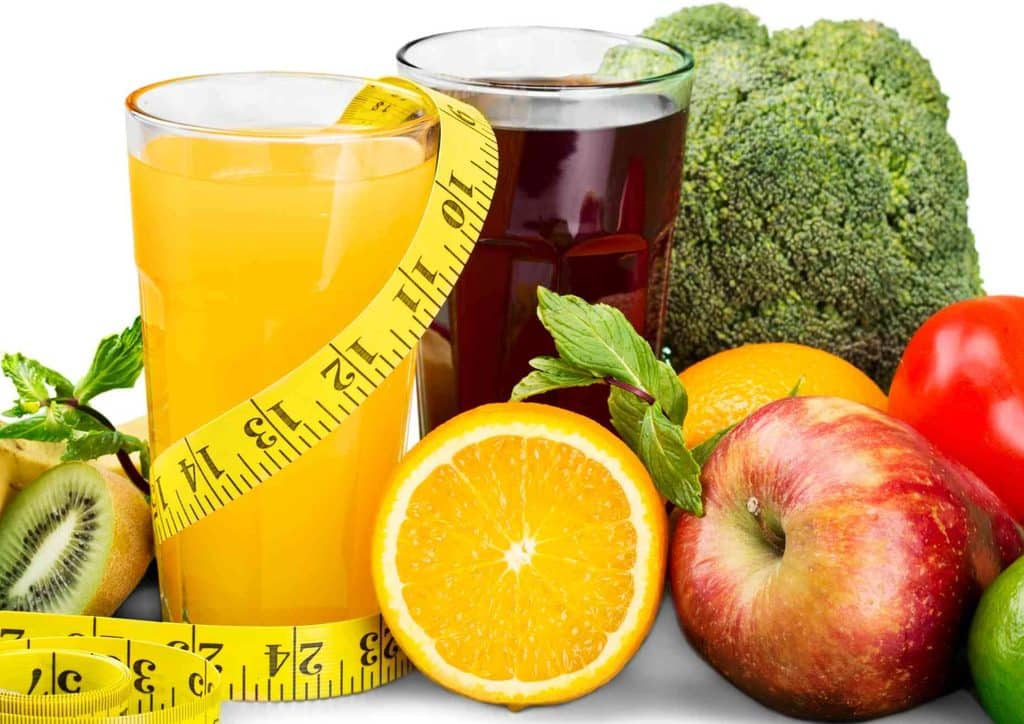 What Is a Balanced Diet for Weight Loss? 21 A vibrant glass of juice with assorted fruits and vegetables alongside a measuring tape, representing healthy lifestyle choices.