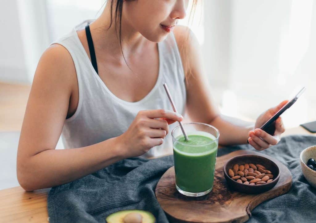 What Is a Balanced Diet for Weight Loss? 20 A woman sits at a table with a green smoothie and a cell phone, appearing focused and engaged in her activity.