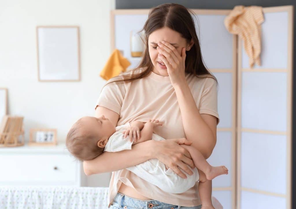 Postpartum Weight Loss: A Gentle, Realistic Guide 31 A woman cradles her baby in her arms, tears streaming down her face, expressing deep emotion and vulnerability.