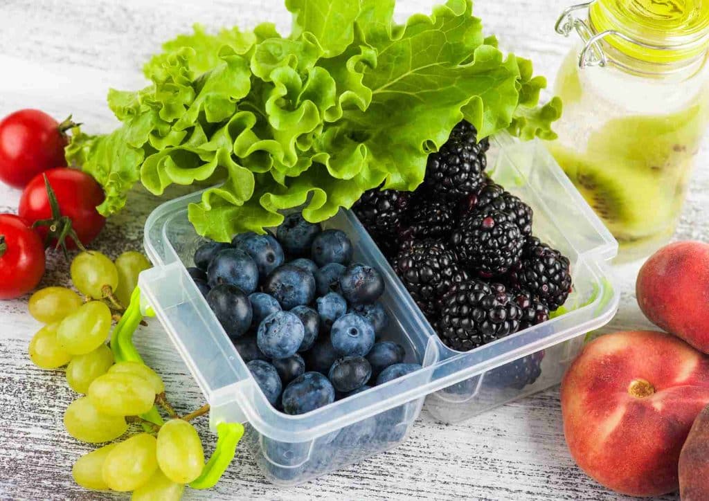 Healthy Snacks for Weight Loss That Actually Keep You Full 13 A plastic container brimming with assorted fruits and vegetables, including apples, carrots, and leafy greens.