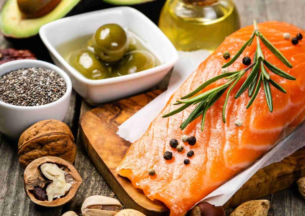 What Is a Balanced Diet for Weight Loss? 3 A wooden cutting board displays salmon, assorted nuts, olives, and various other foods arranged attractively.