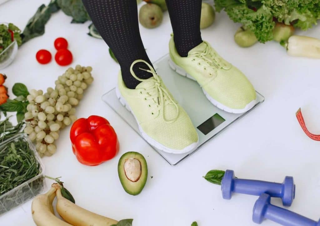 Losing Weight While Breastfeeding: What's Safe and Realistic 34 A person stands on a scale, surrounded by an assortment of fresh fruits and vegetables, promoting healthy living.