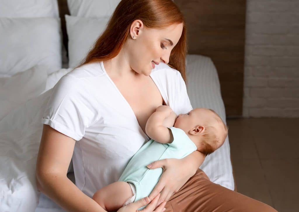 Losing Weight While Breastfeeding: What's Safe and Realistic 70 A woman sits on a bed, cradling her baby in her arms, both appearing calm and content.