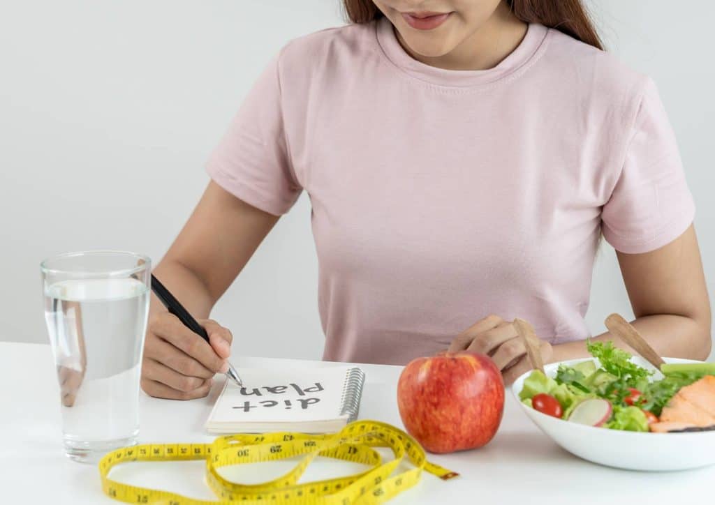 Is the Mediterranean Diet Good for Weight Loss? 10 A woman writes in a notebook while holding a measuring tape, focused on her task.