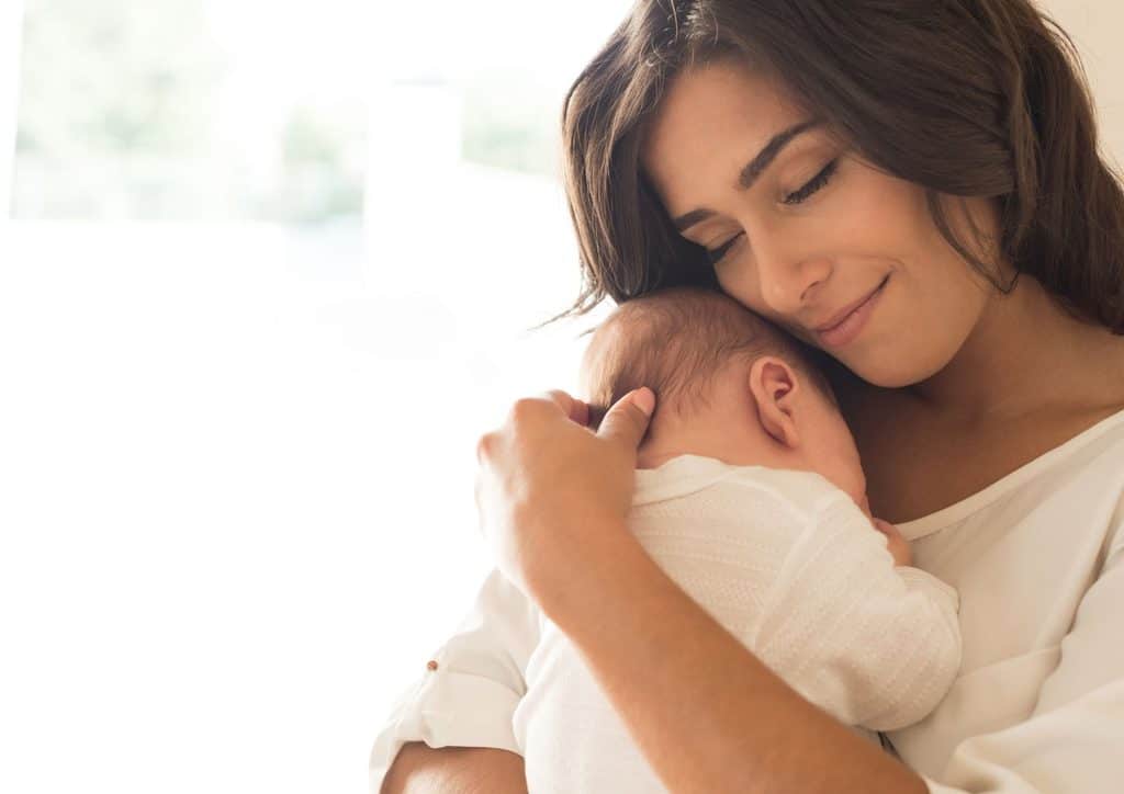 Losing Weight While Breastfeeding: What's Safe and Realistic 12 A woman smiles while holding a baby in her arms, showcasing a moment of joy and affection.
