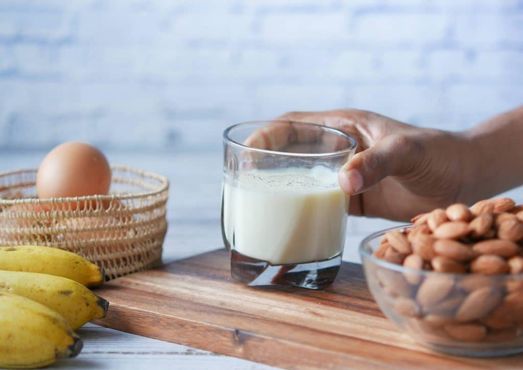 Is Whey Protein Good for Weight Loss? 16 A person holds a glass of milk in one hand and a bowl of almonds in the other, showcasing a healthy snack choice.