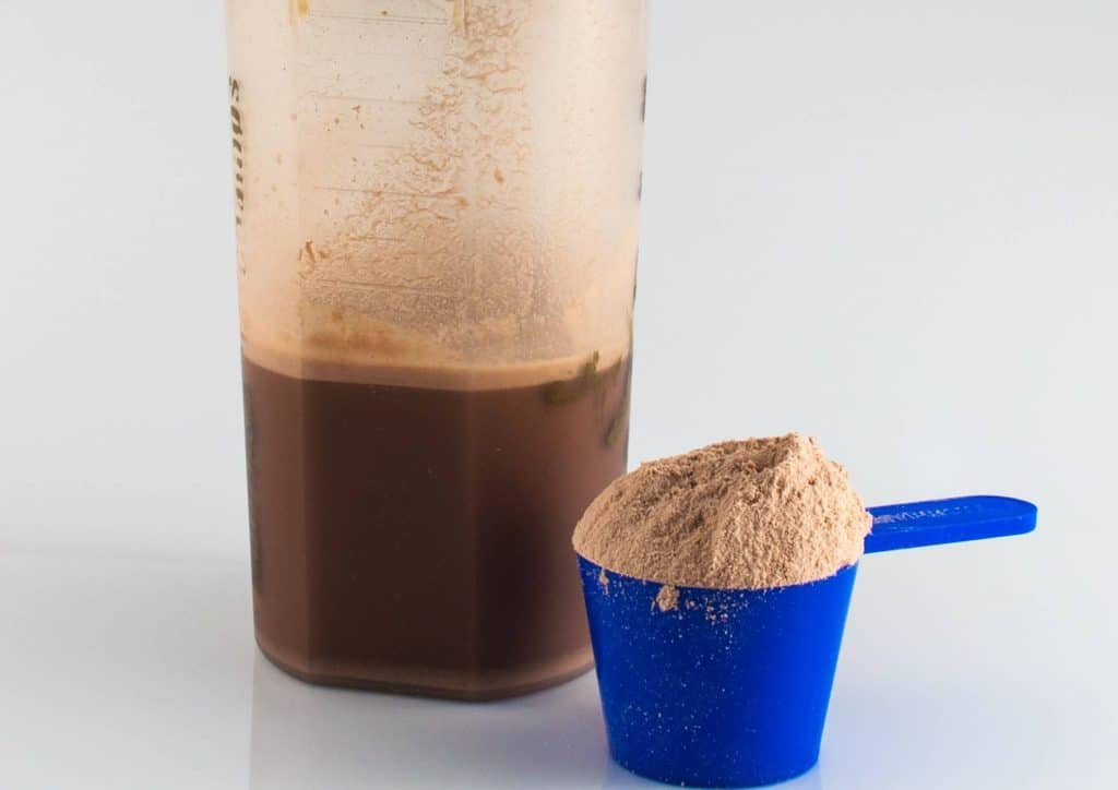 Is Whey Protein Good for Weight Loss? 12 Chocolate protein powder in a clear container with a scoop, placed on a wooden surface.