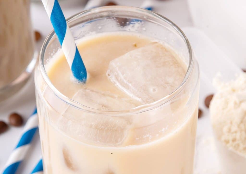 Is Whey Protein Good for Weight Loss? 10 Iced coffee in a clear glass with ice cubes and a blue and white striped straw.
