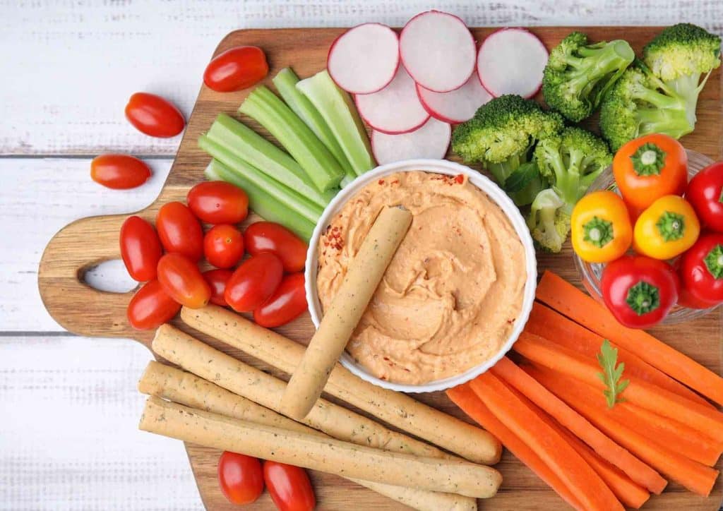 High Fibre Diet for Weight Loss: Why Fibre Keeps You Full 8 A cutting board featuring a variety of fresh vegetables arranged with a small bowl of dip in the cente.