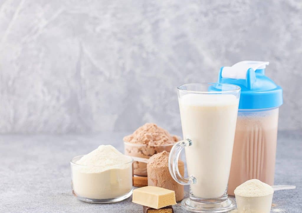 Is Whey Protein Good for Weight Loss? 9 Protein powder and various ingredients arranged on a gray background, showcasing a healthy nutrition setup.