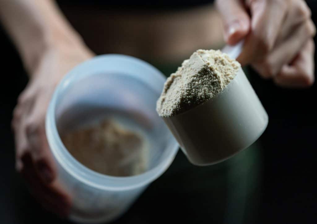 Is Whey Protein Good for Weight Loss? 5 A person holding a container of protein powder, showcasing the product's label and their hand gripping the lid.